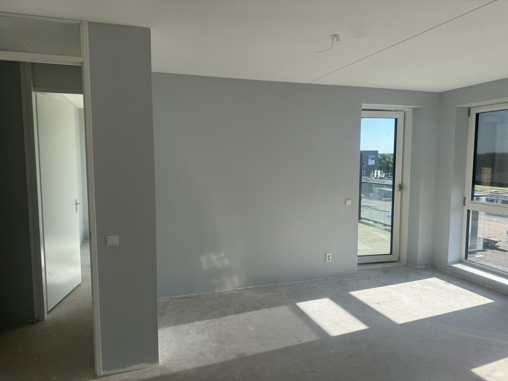 Lege kamer in een nieuw appartement met balkondeur, betonvloer en wanden die klaar zijn voor de afwerking