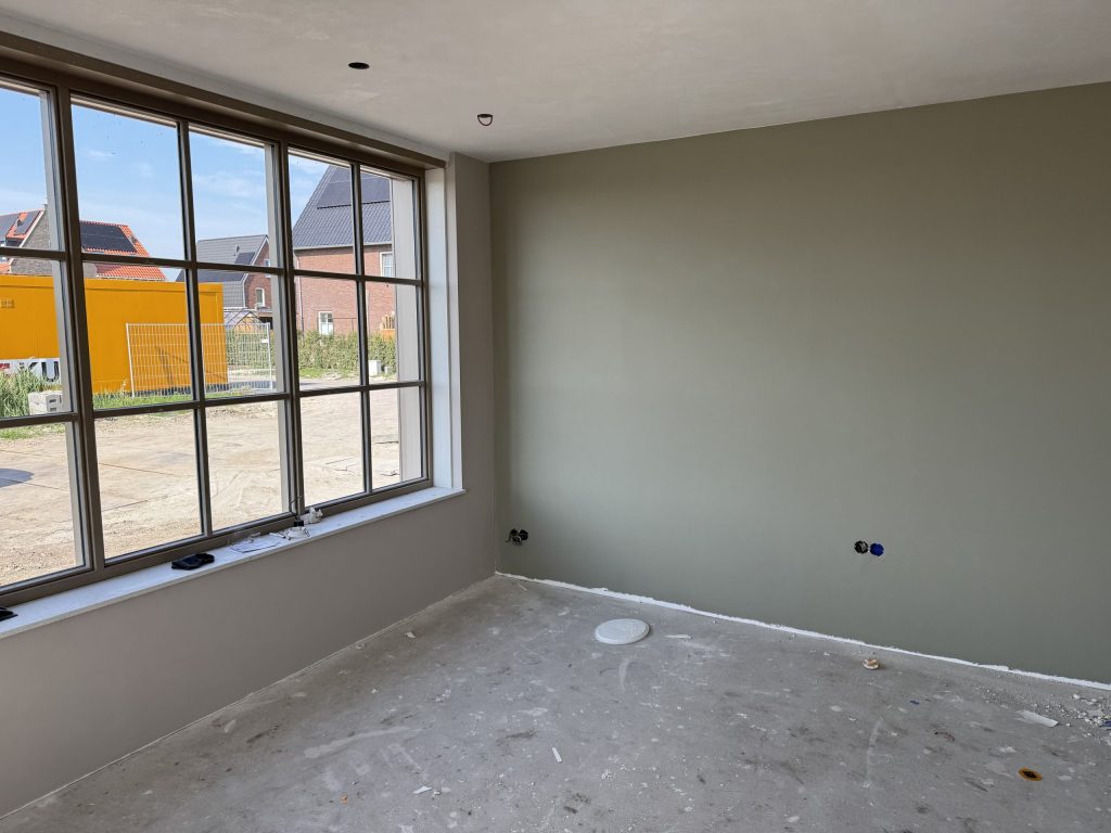 Kamer in een nieuw huis met een grote raampartij en een egaal afgewerkte groengrijze wand