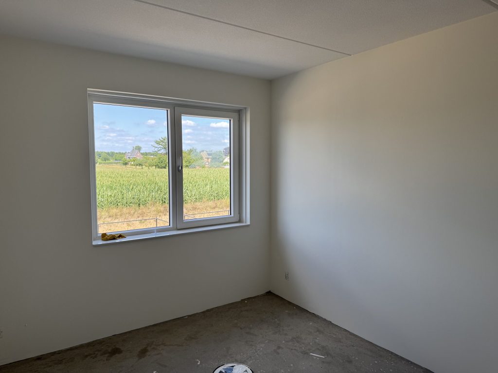 Lege nieuwbouwkamer met gladde lichte wanden en een raam met uitzicht op een veld